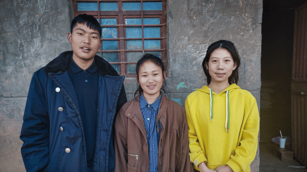 Three people stand together in front of a large building, smiling and looking towards the camera.