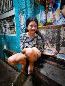 Girl smiling and sitting by a small store in a dark alley