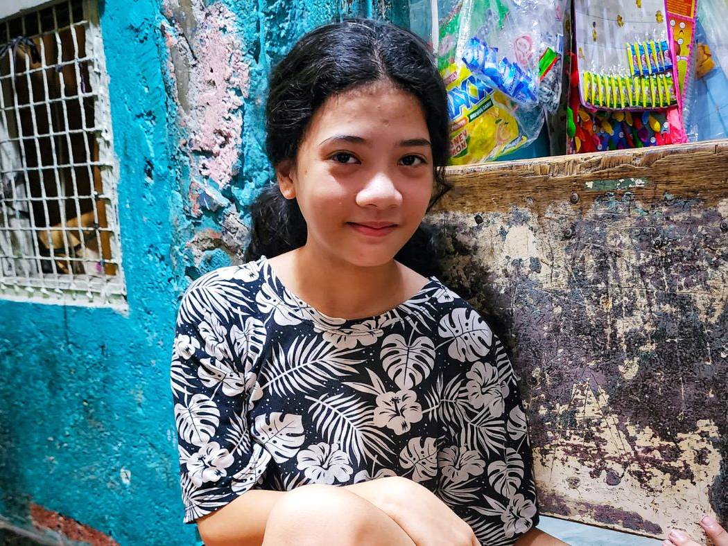 Girl smiling and sitting by a small store in a dark alley