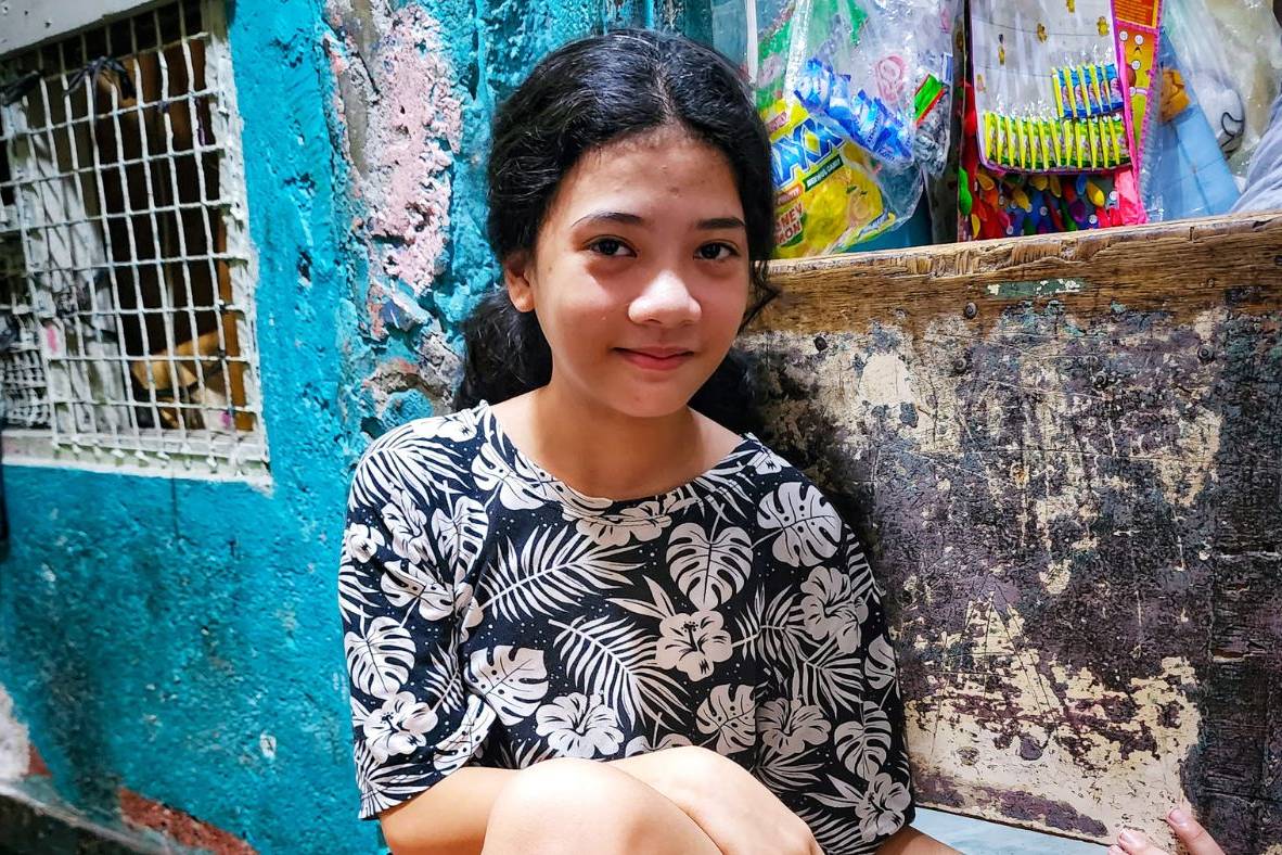 Girl smiling and sitting by a small store in a dark alley