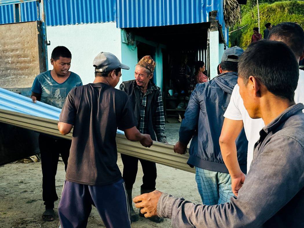 Local residents assist the response team in moving roofing sets for distribution.