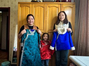 Chinese woman, her daughter, and another chinese woman posing for a photo while holding clothes sewn by the first woman.