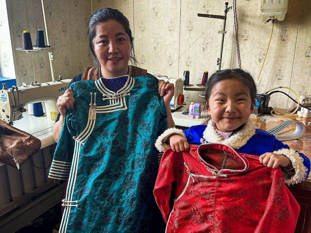 Chinese woman, her daughter posing for a photo while holding clothes sewn by the woman.