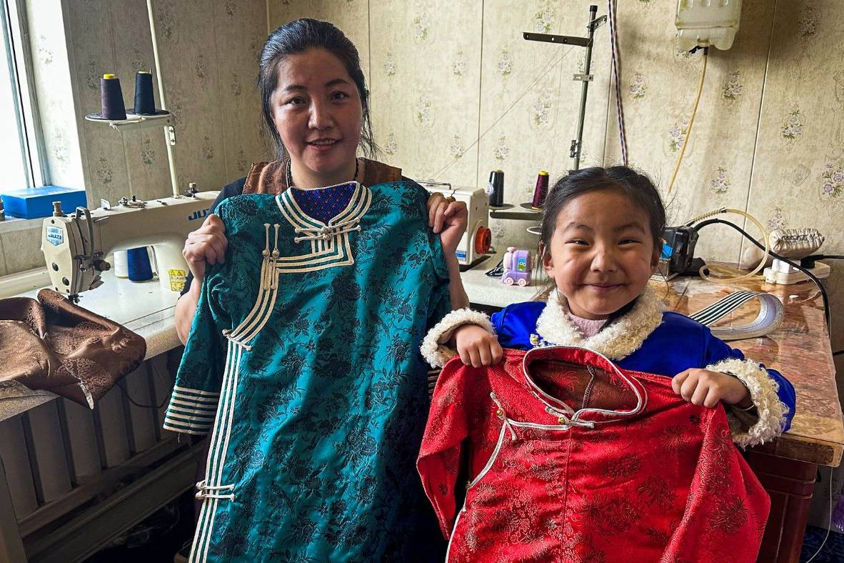 Chinese woman, her daughter posing for a photo while holding clothes sewn by the woman.