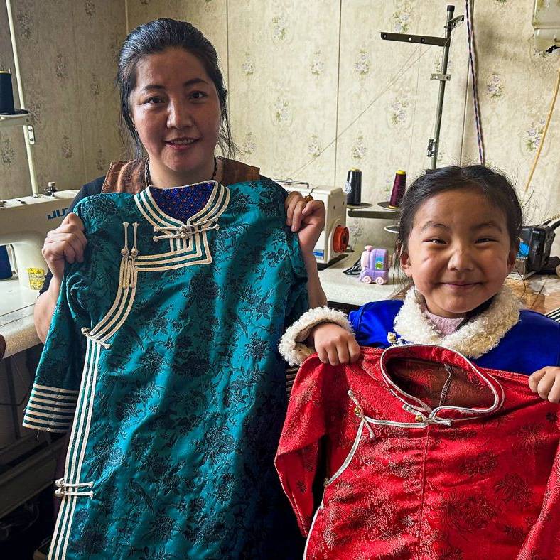 Chinese woman, her daughter posing for a photo while holding clothes sewn by the woman.