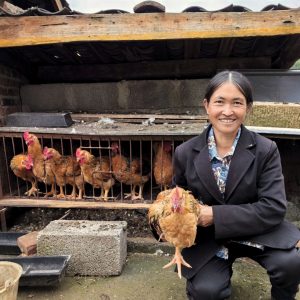 Chinese woman sitting down while holding one of her chickens