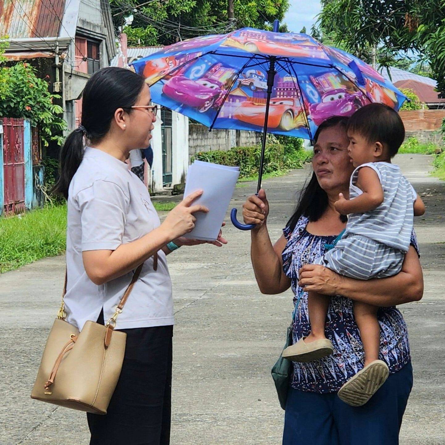 Filipino staff member talking to a mother carrying her child.