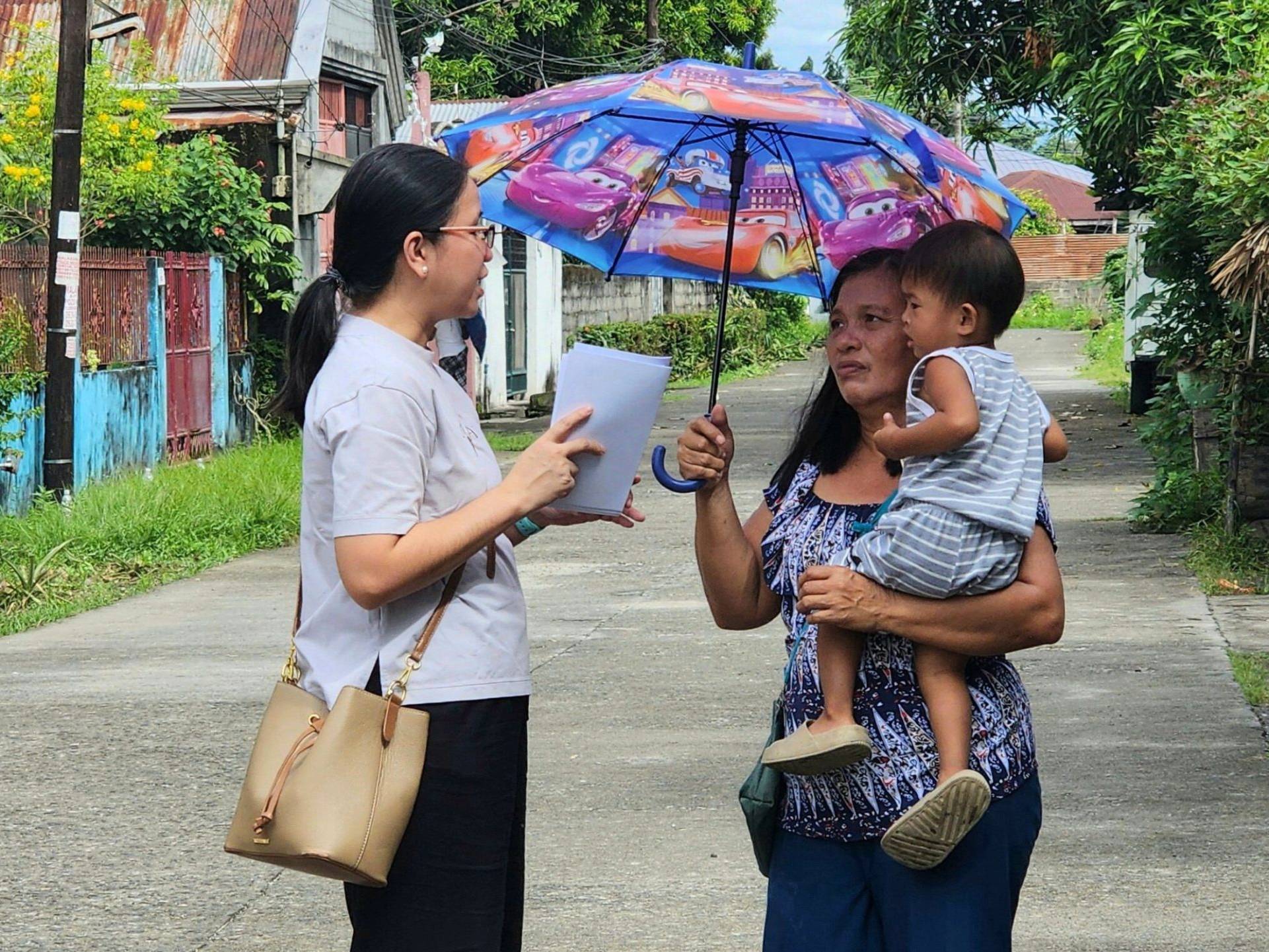 Filipino staff member talking to a mother carrying her child.