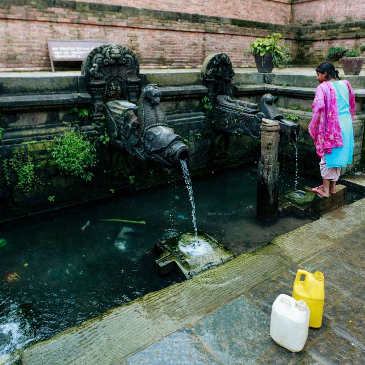 A girl in colorful clothing collecting water from an ornate public tap.