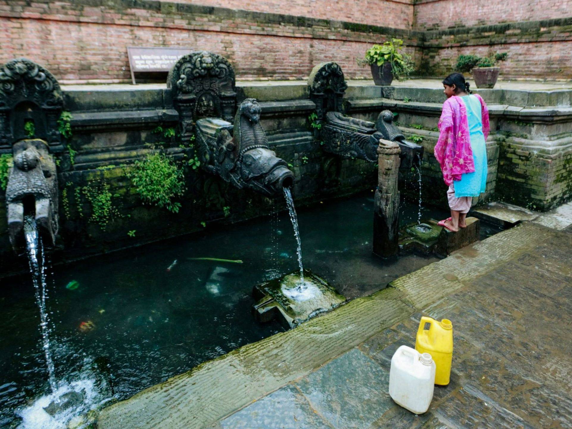 A girl in colorful clothing collecting water from an ornate public tap.