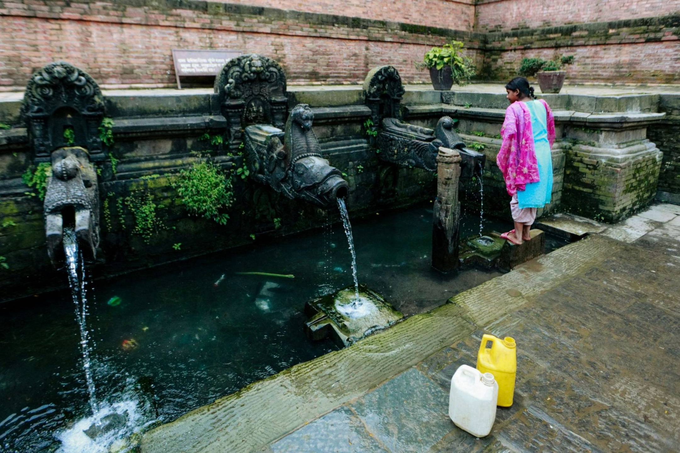 A girl in colorful clothing collecting water from an ornate public tap.