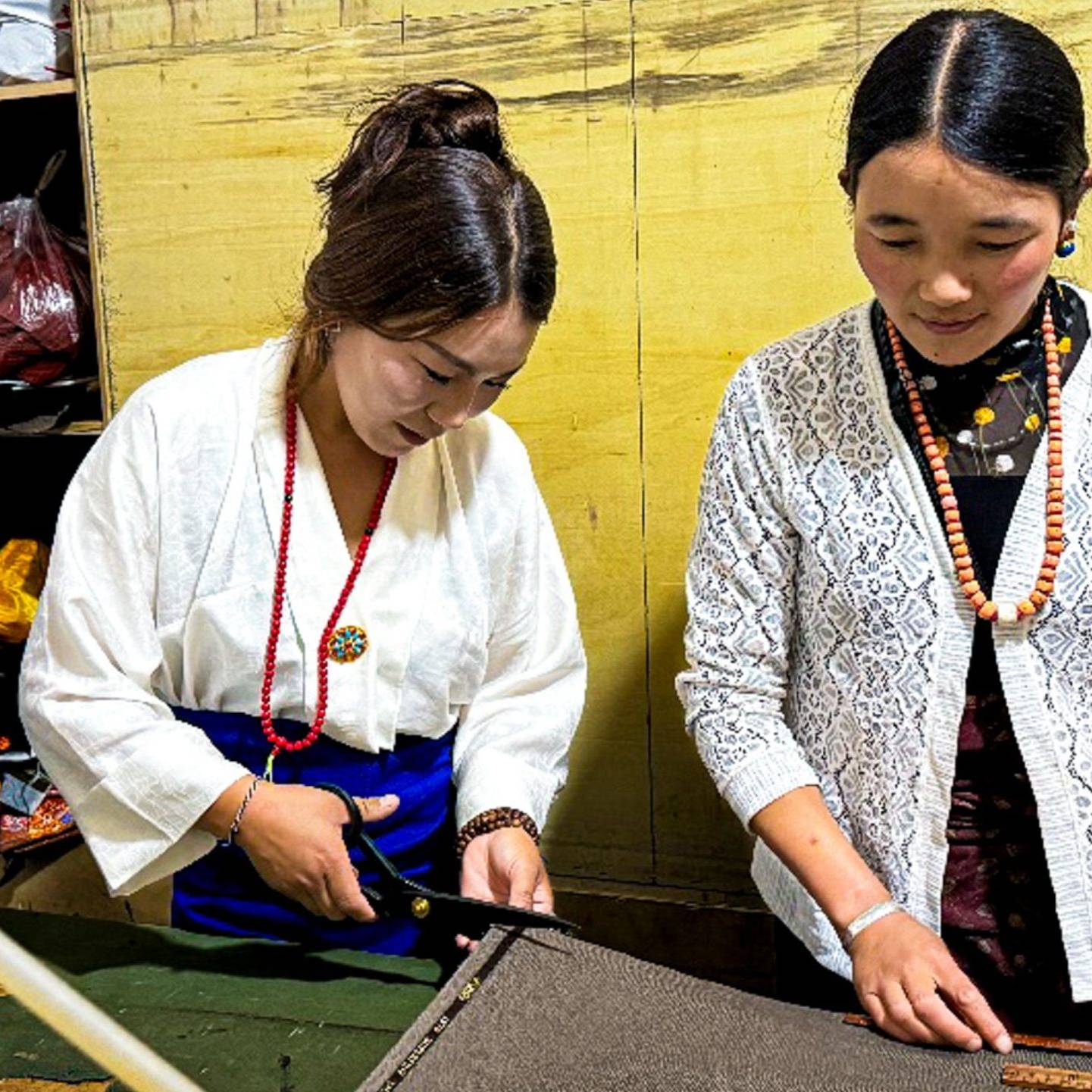 Woman measuring and cutting fabric while another woman assists her.