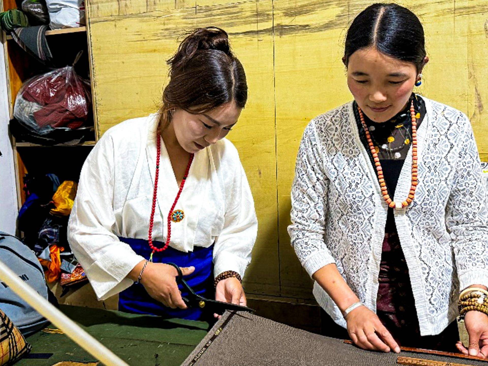 Woman measuring and cutting fabric while another woman assists her.