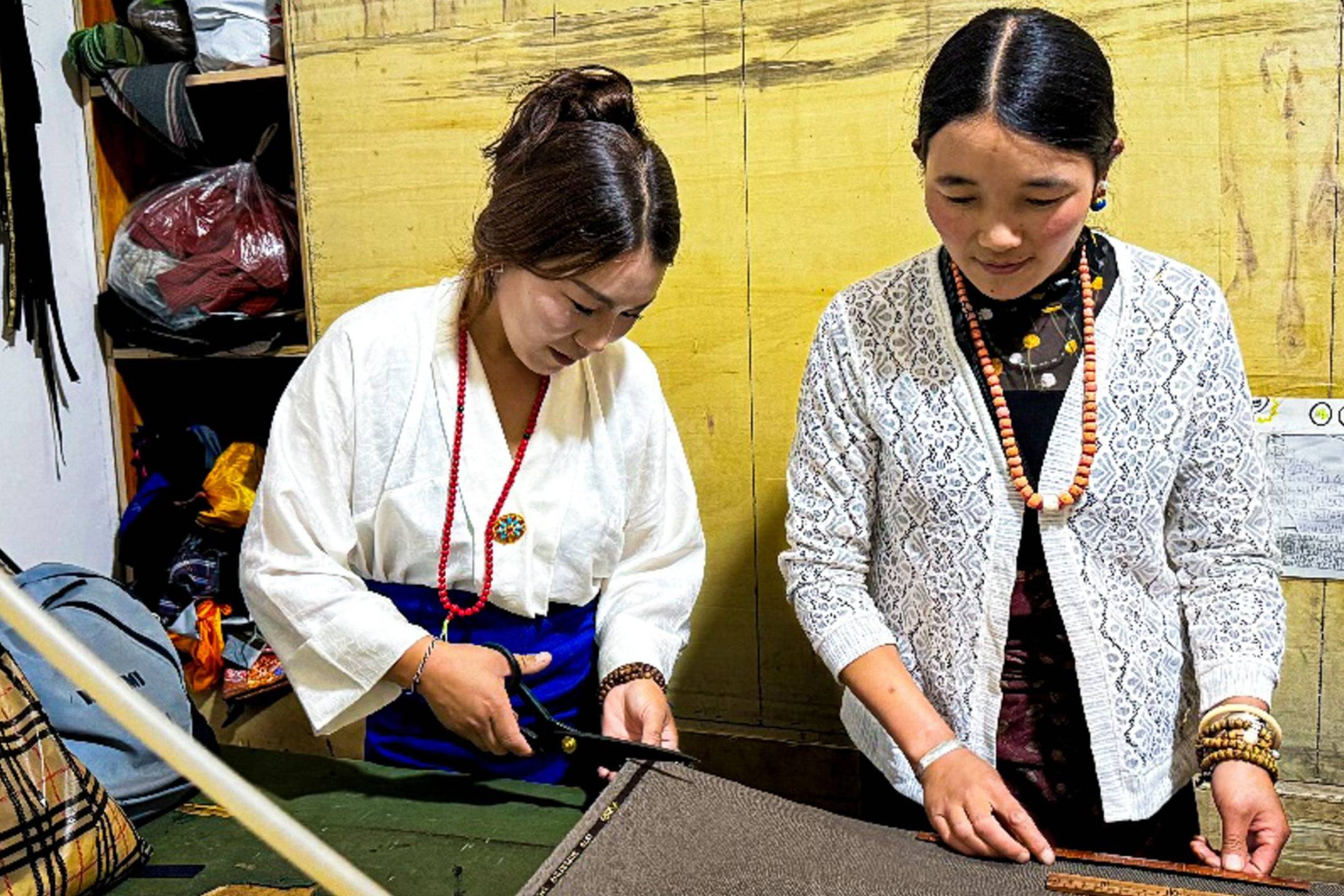 Woman measuring and cutting fabric while another woman assists her.