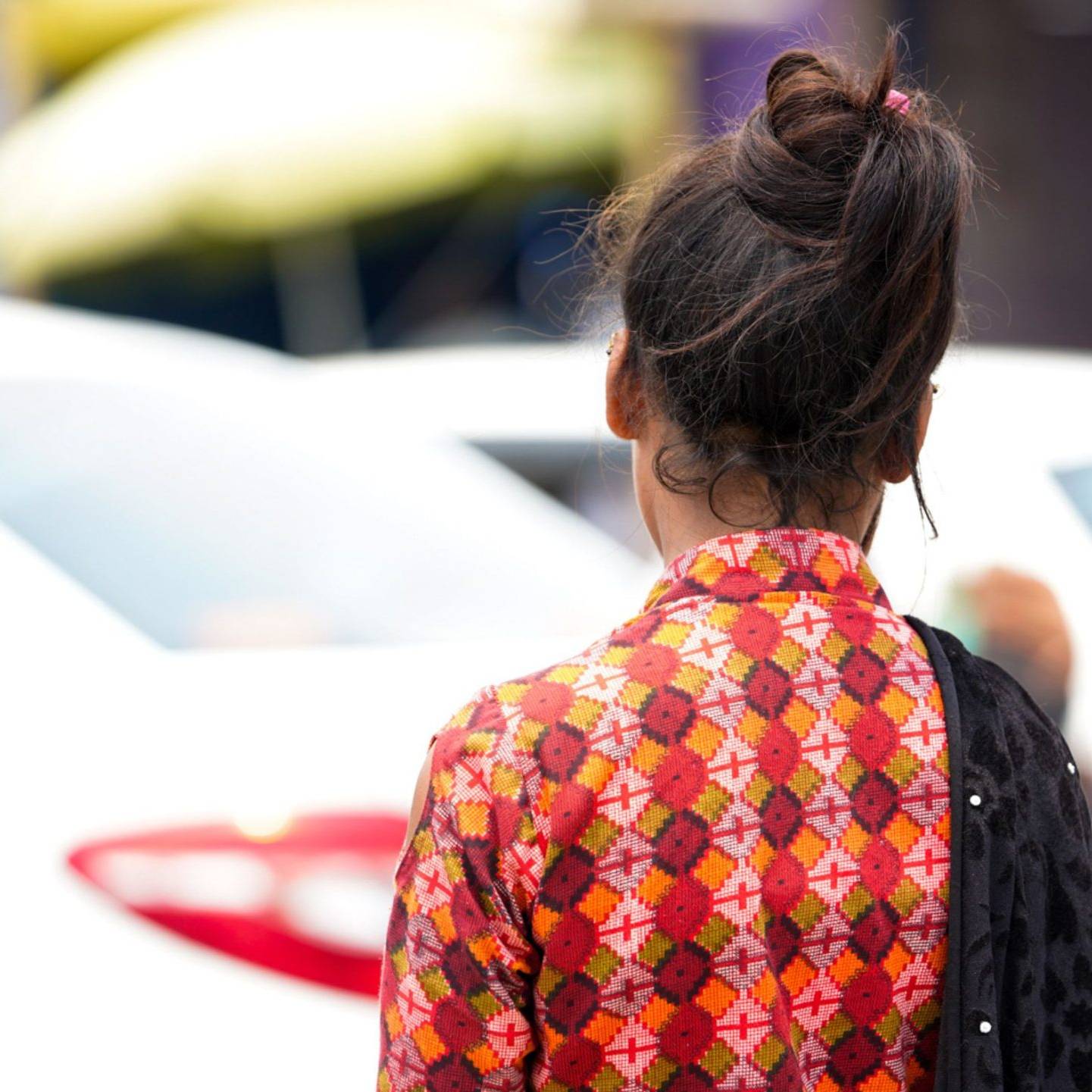 A woman in a patterned dress stands with her back to the camera, surrounded by a busy urban setting.