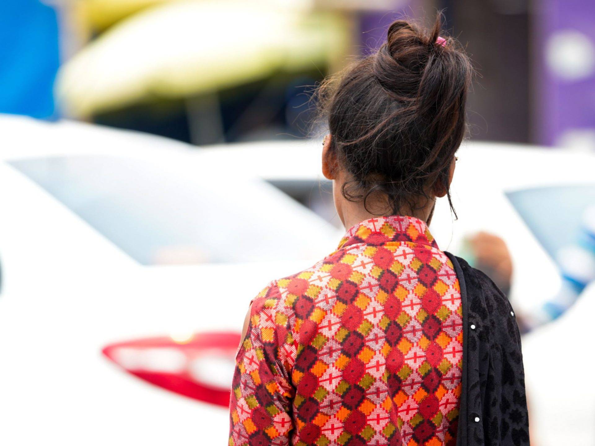 A woman in a patterned dress stands with her back to the camera, surrounded by a busy urban setting.