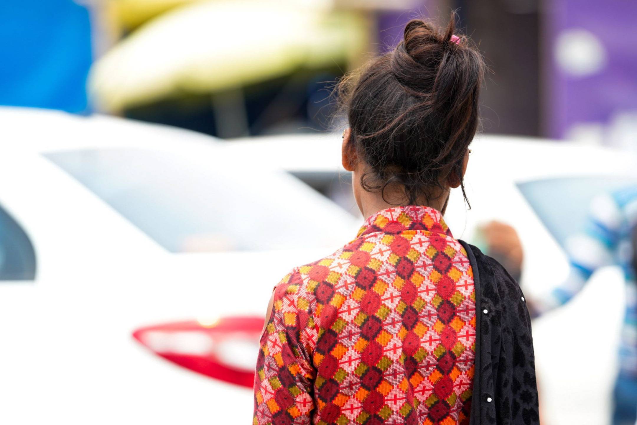 A woman in a patterned dress stands with her back to the camera, surrounded by a busy urban setting.