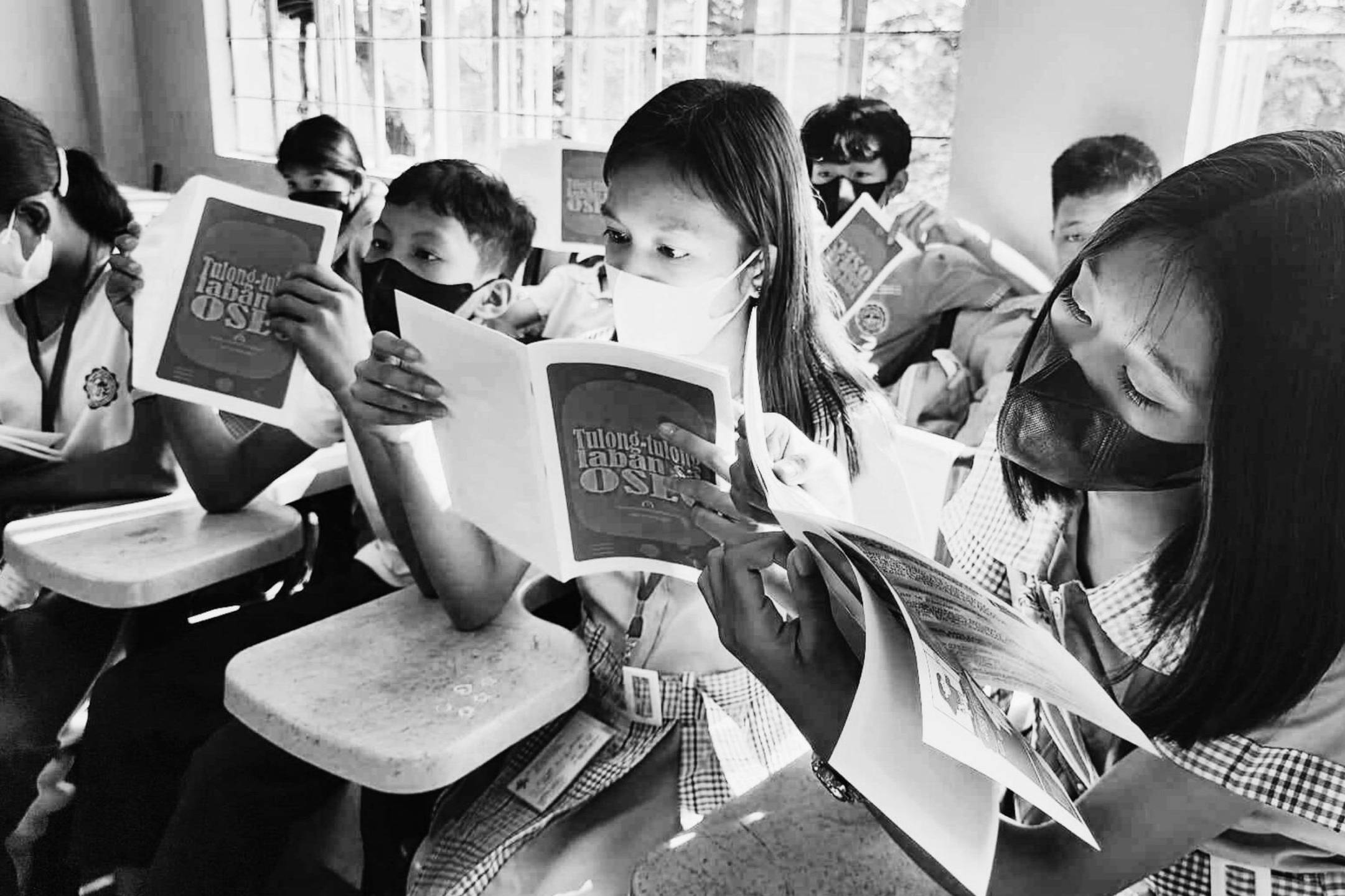 Students in a classroom attentively reading materials about online safety.