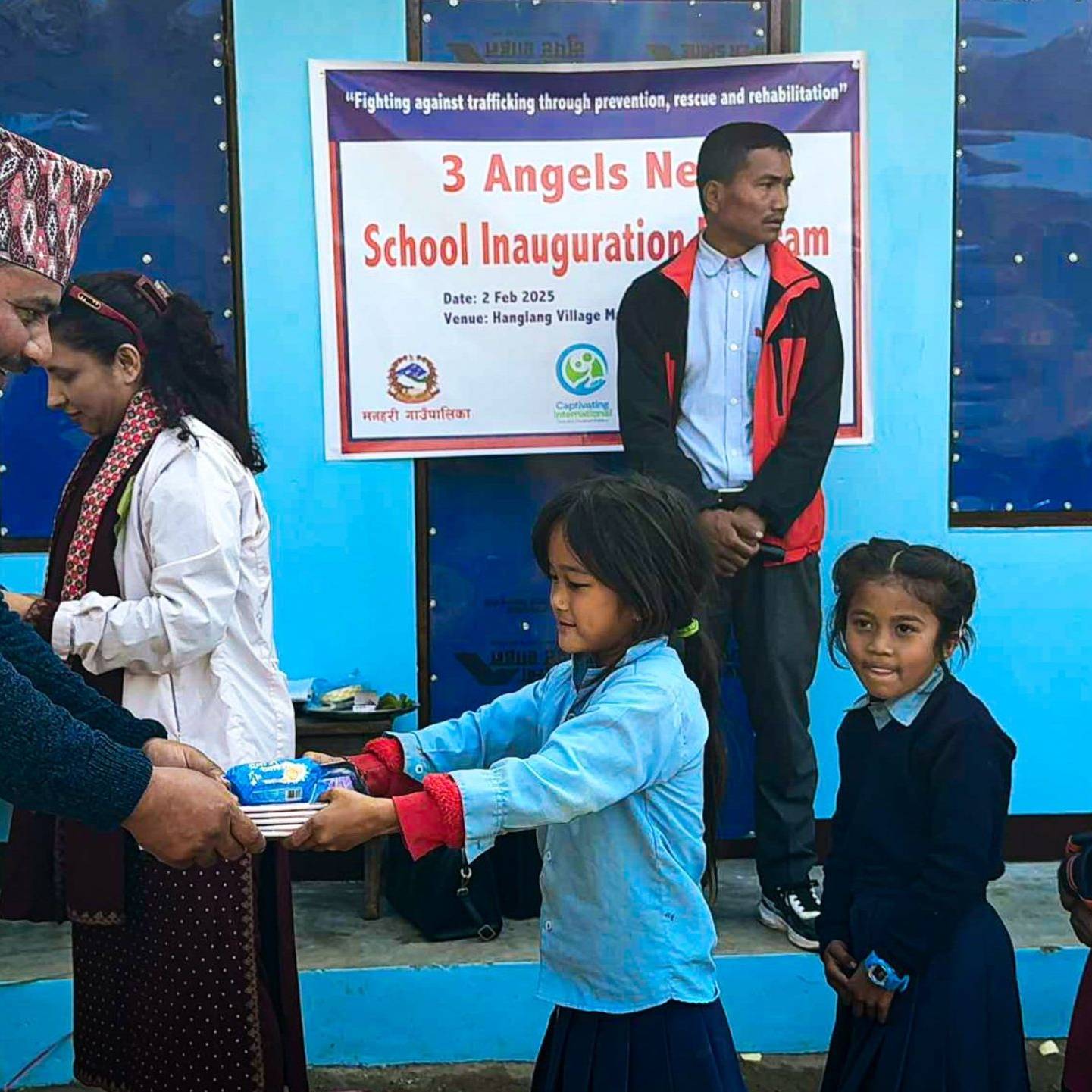 A young girl receives supplies at the inauguration of a school in Hanglang, with community members celebrating the event.