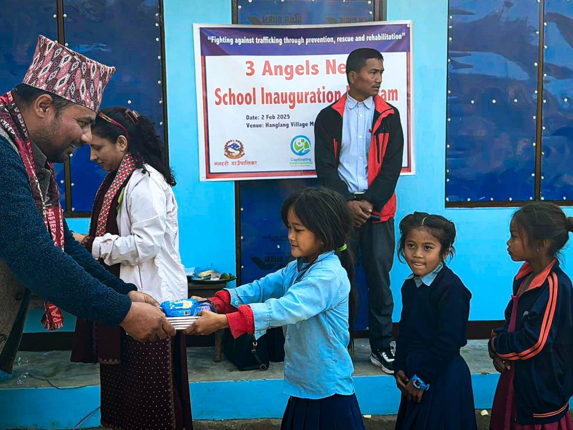 A young girl receives supplies at the inauguration of a school in Hanglang, with community members celebrating the event.