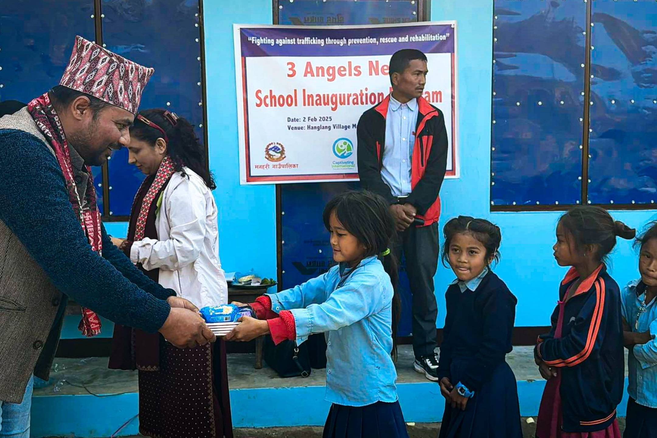 A young girl receives supplies at the inauguration of a school in Hanglang, with community members celebrating the event.