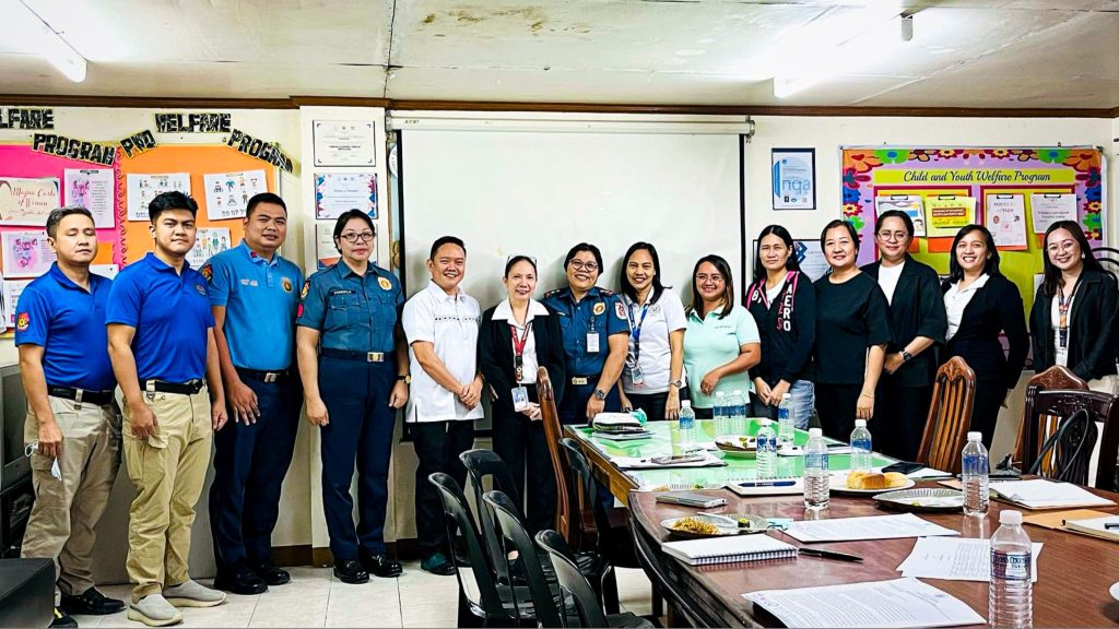 A group of police officers, government officials, and social workers pose together in a meeting room.