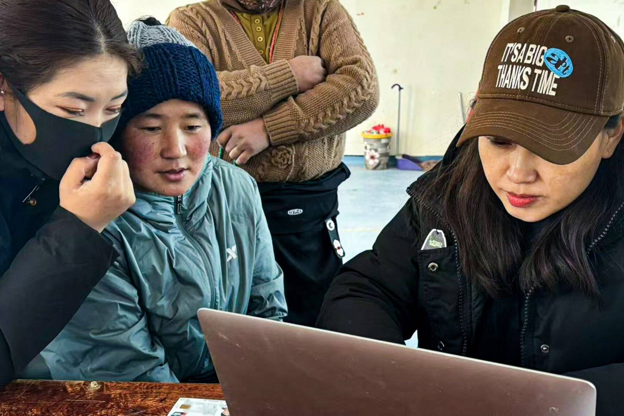 A diverse group of individuals gathered around a laptop, engaged in discussion.