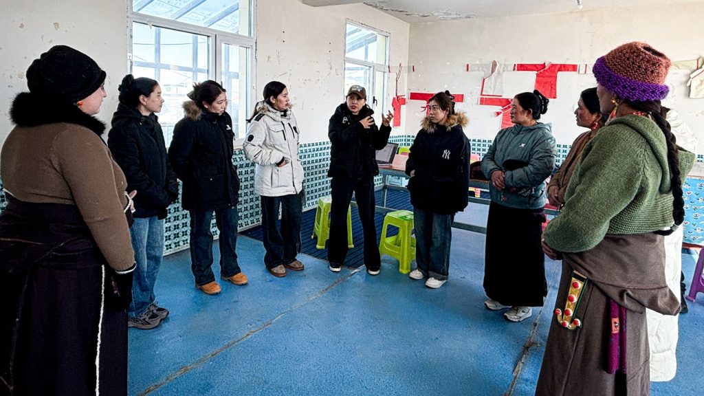 A group discussion taking place in a room, with women standing in a circle, listening to one speaker.