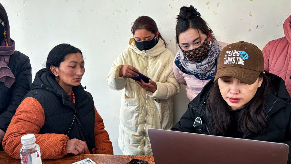 A diverse group of individuals gathered around a laptop, engaged in discussion.