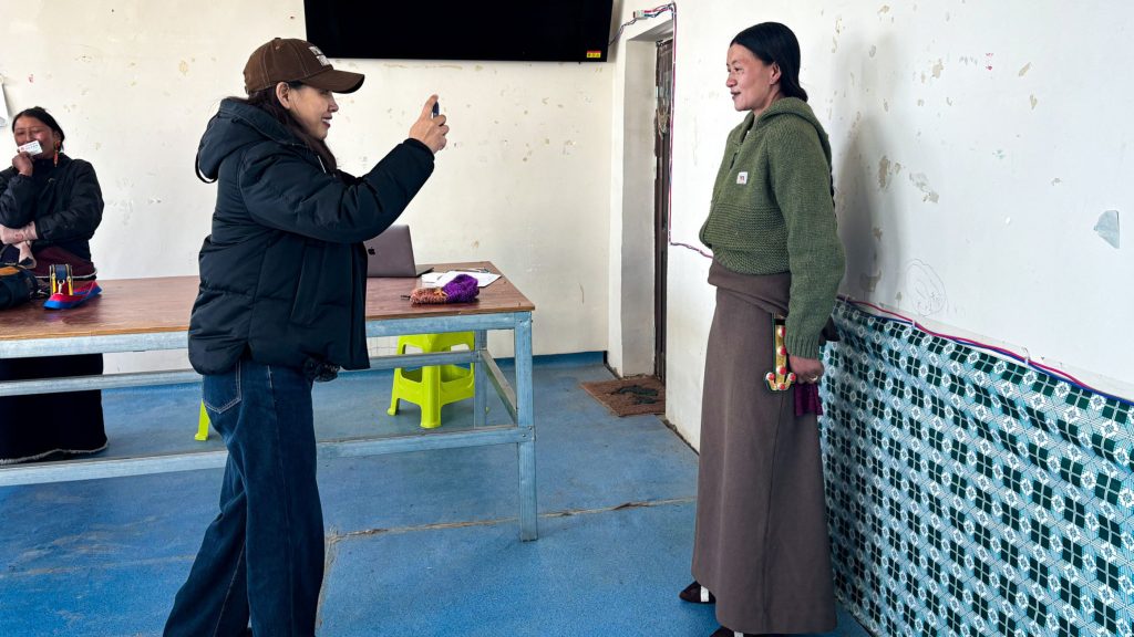 A woman capturing a photo of another woman in a well-lit room.