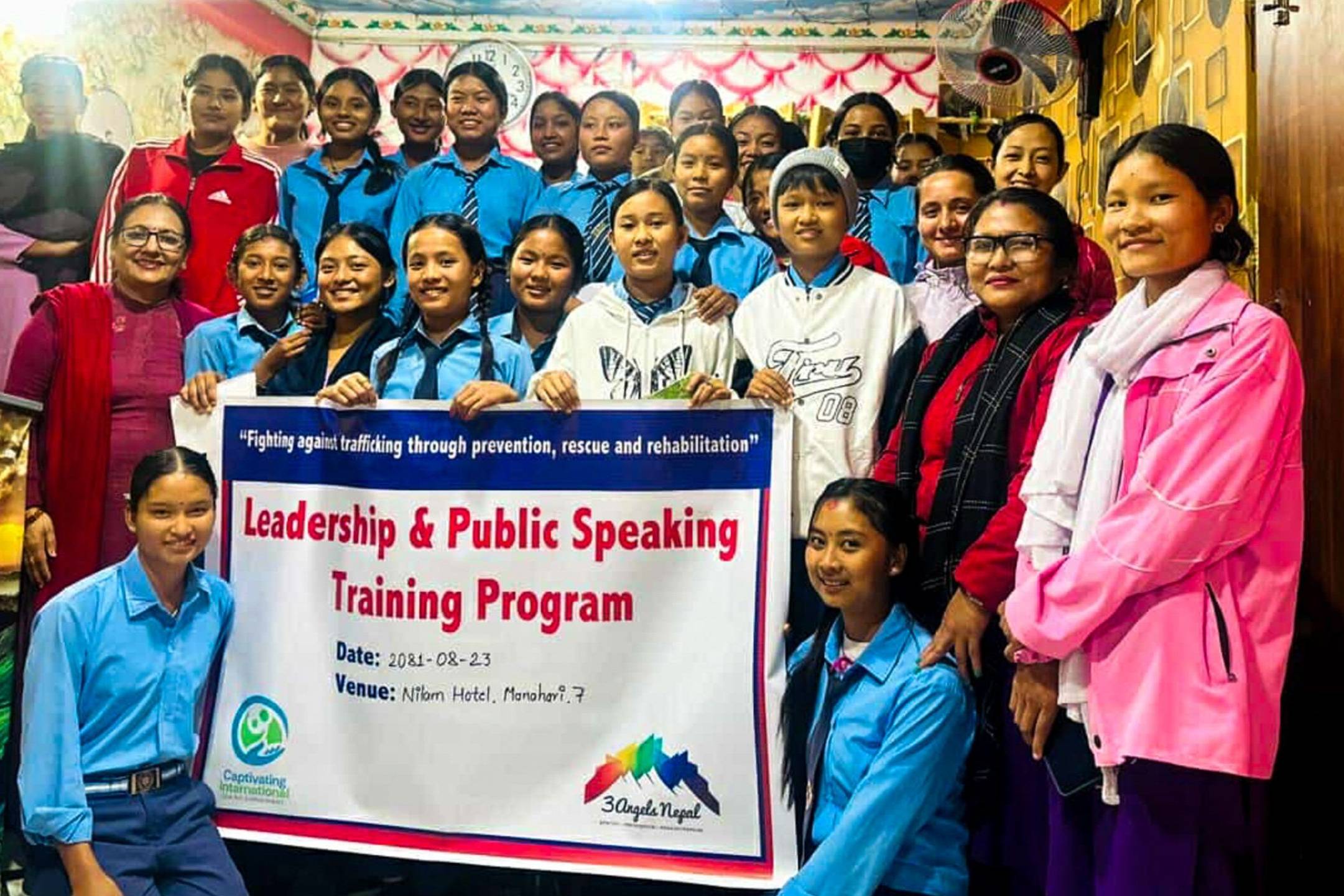 A group of girls and trainers posing with a banner for the Leadership & Public Speaking Training Program.