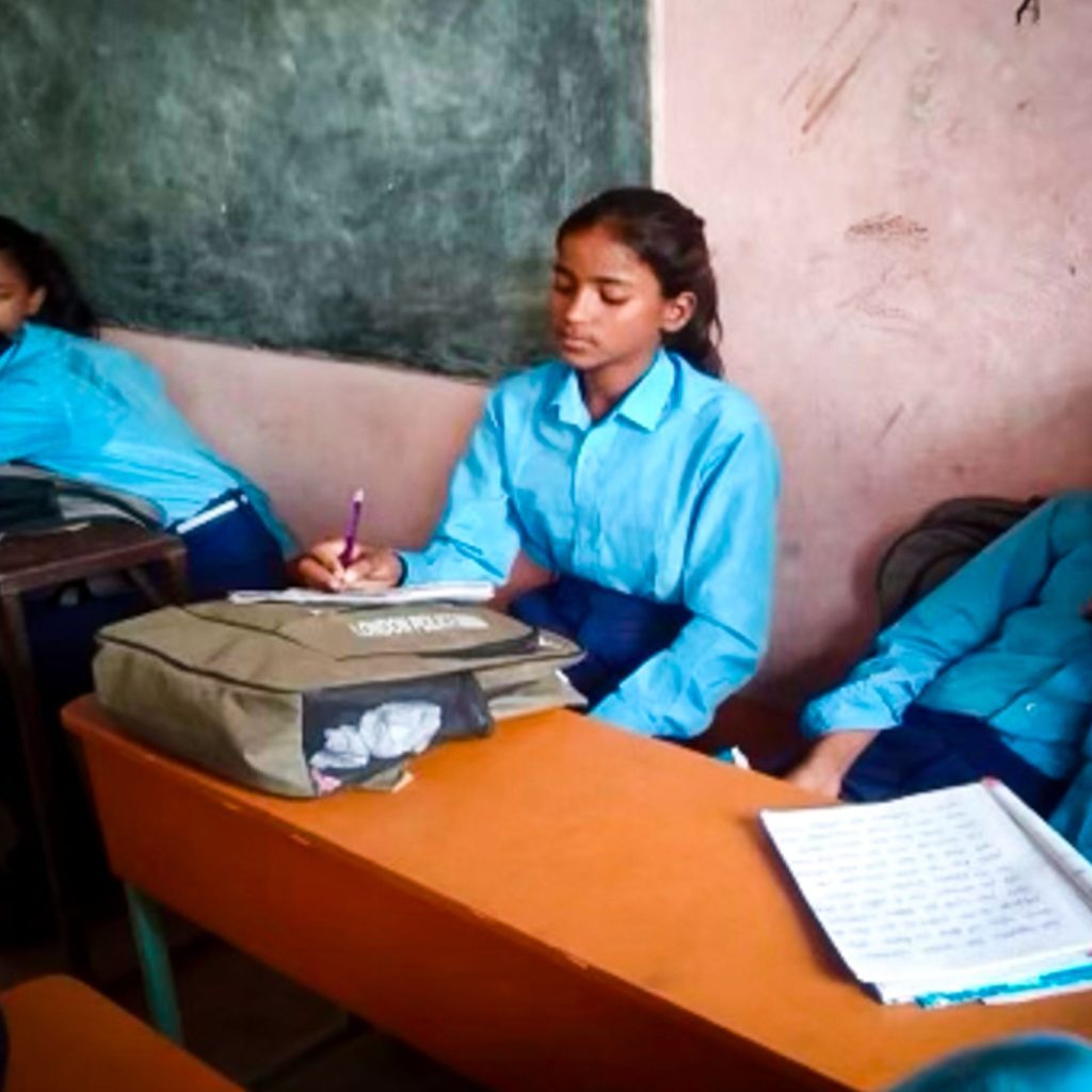 A schoolgirl in a blue uniform attentively writing in class.