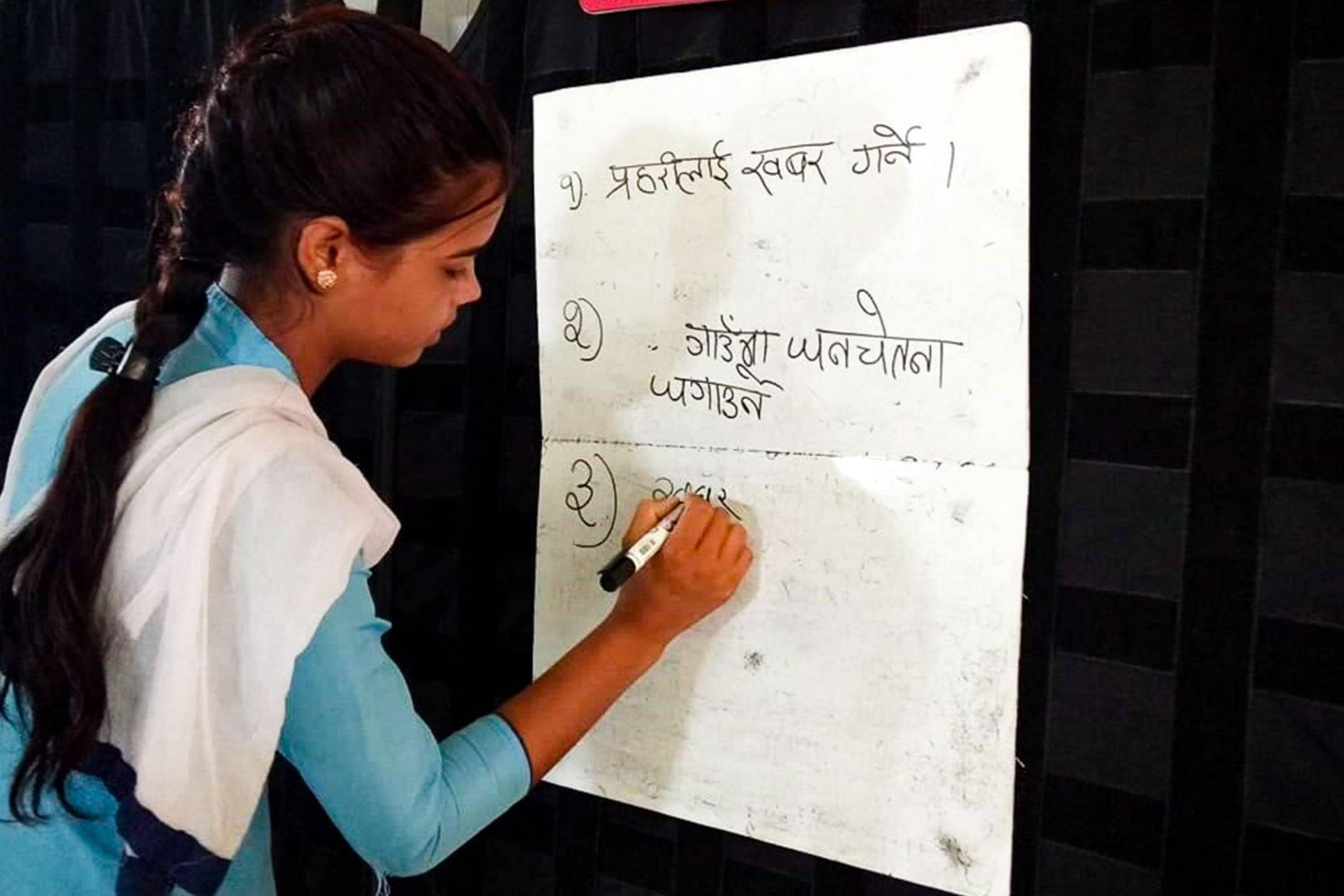 A schoolgirl writing on a chart during a lesson.