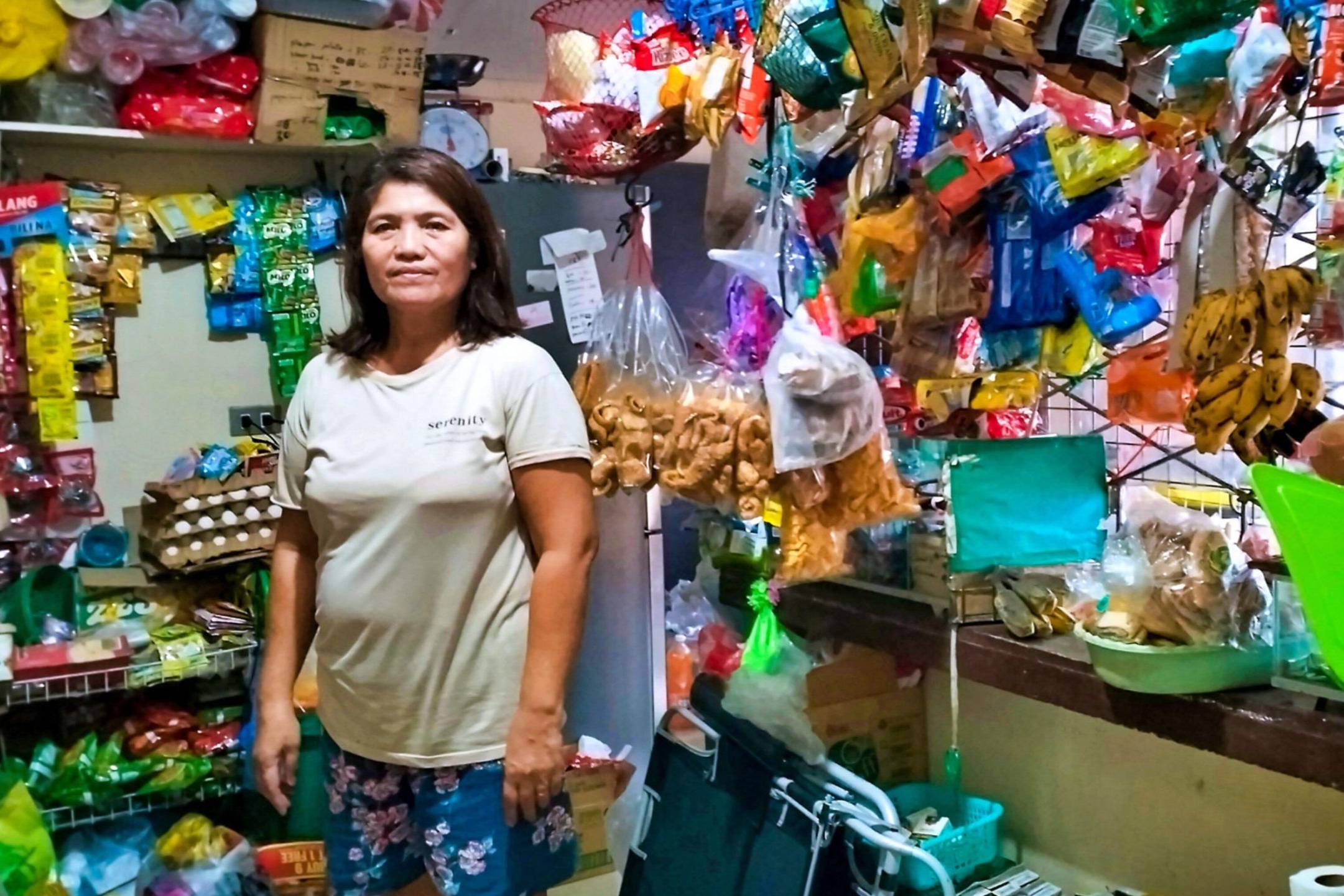 A woman stands proudly in her small variety store.