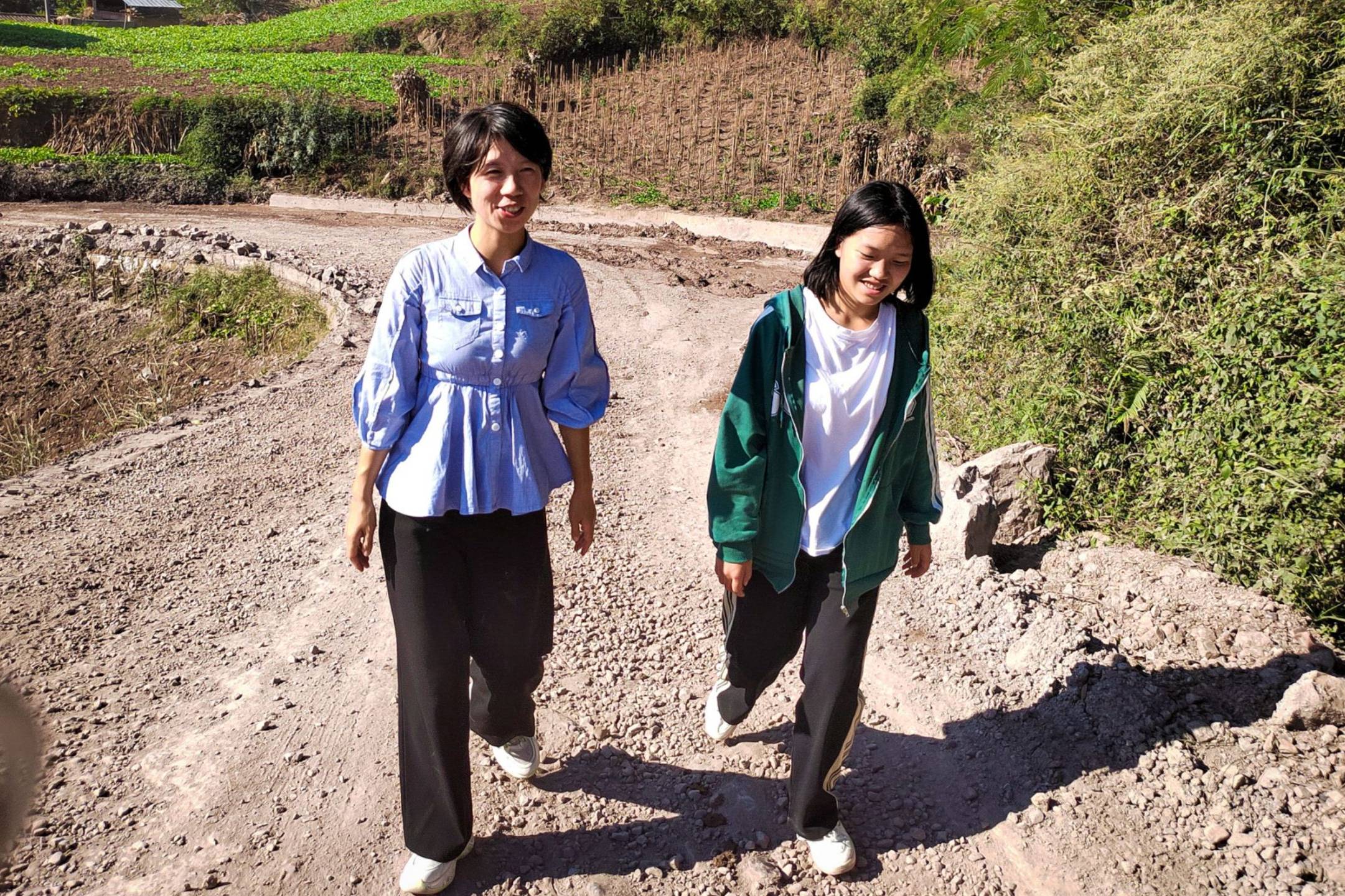 Two women walking on a dirt road.