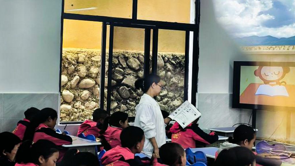 A classroom scene featuring children at desks, with a teacher engaging with the students.