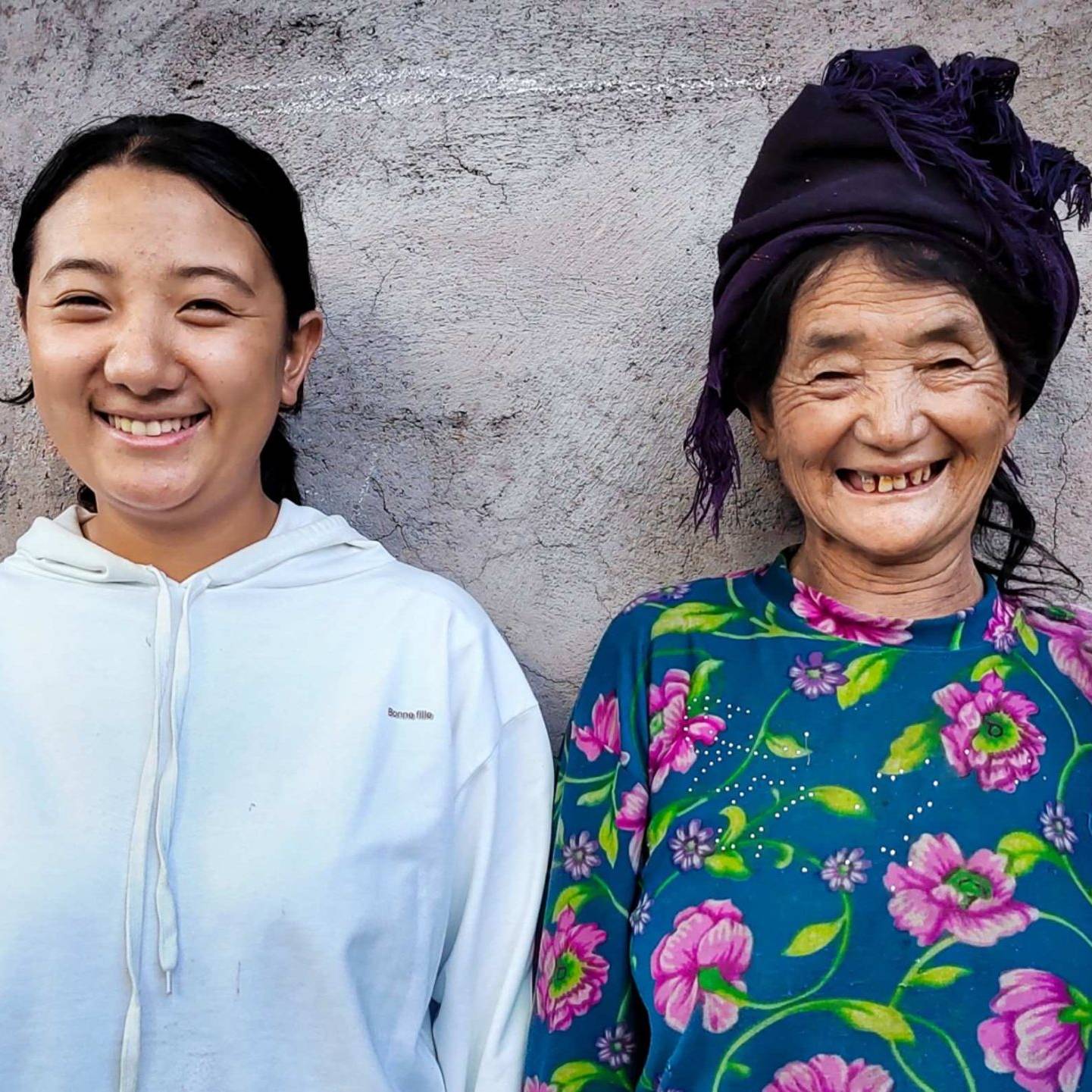 Two women standing next to each other, both smiling warmly and radiating positivity.