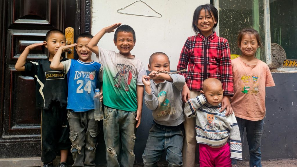 Several children standing close together, smiling for a group picture in a sunny setting.