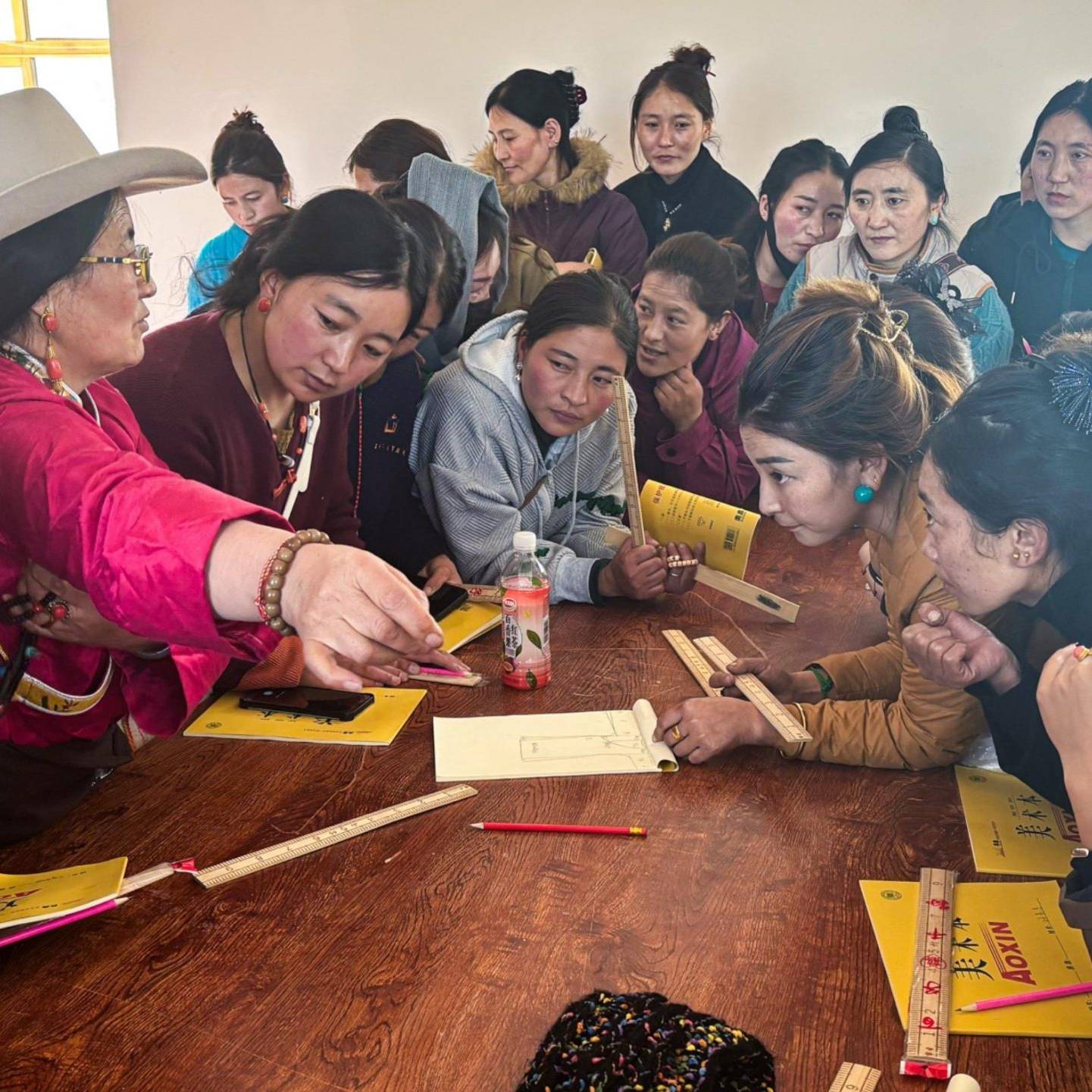 Women are seated around a table with papers, engaged in conversation and collaboration on a project or activity.