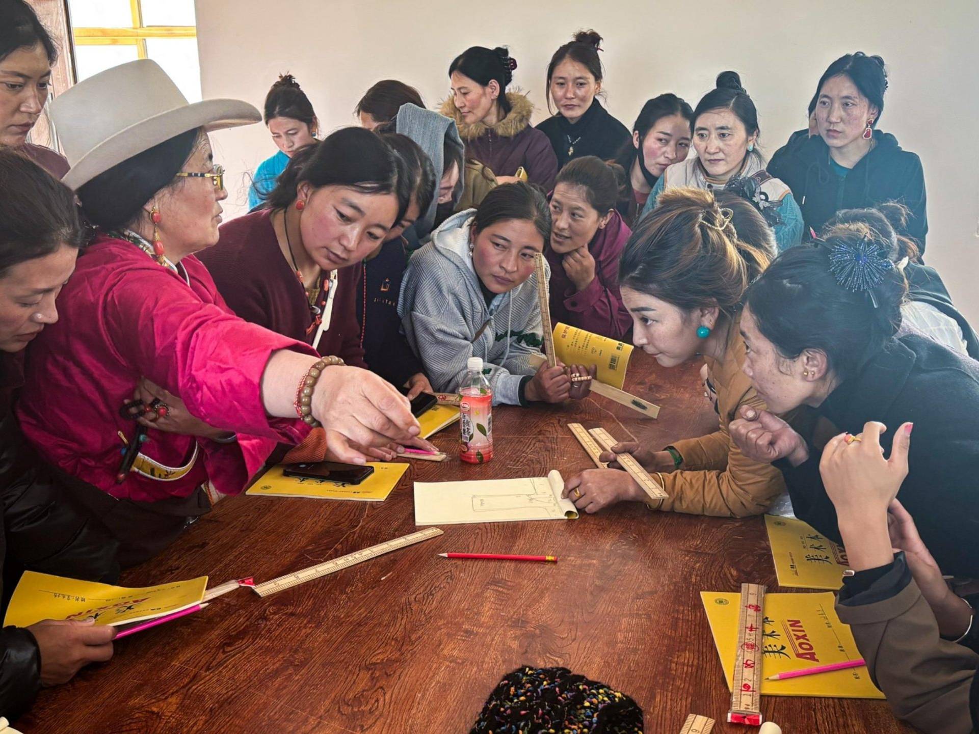 Women are seated around a table with papers, engaged in conversation and collaboration on a project or activity.