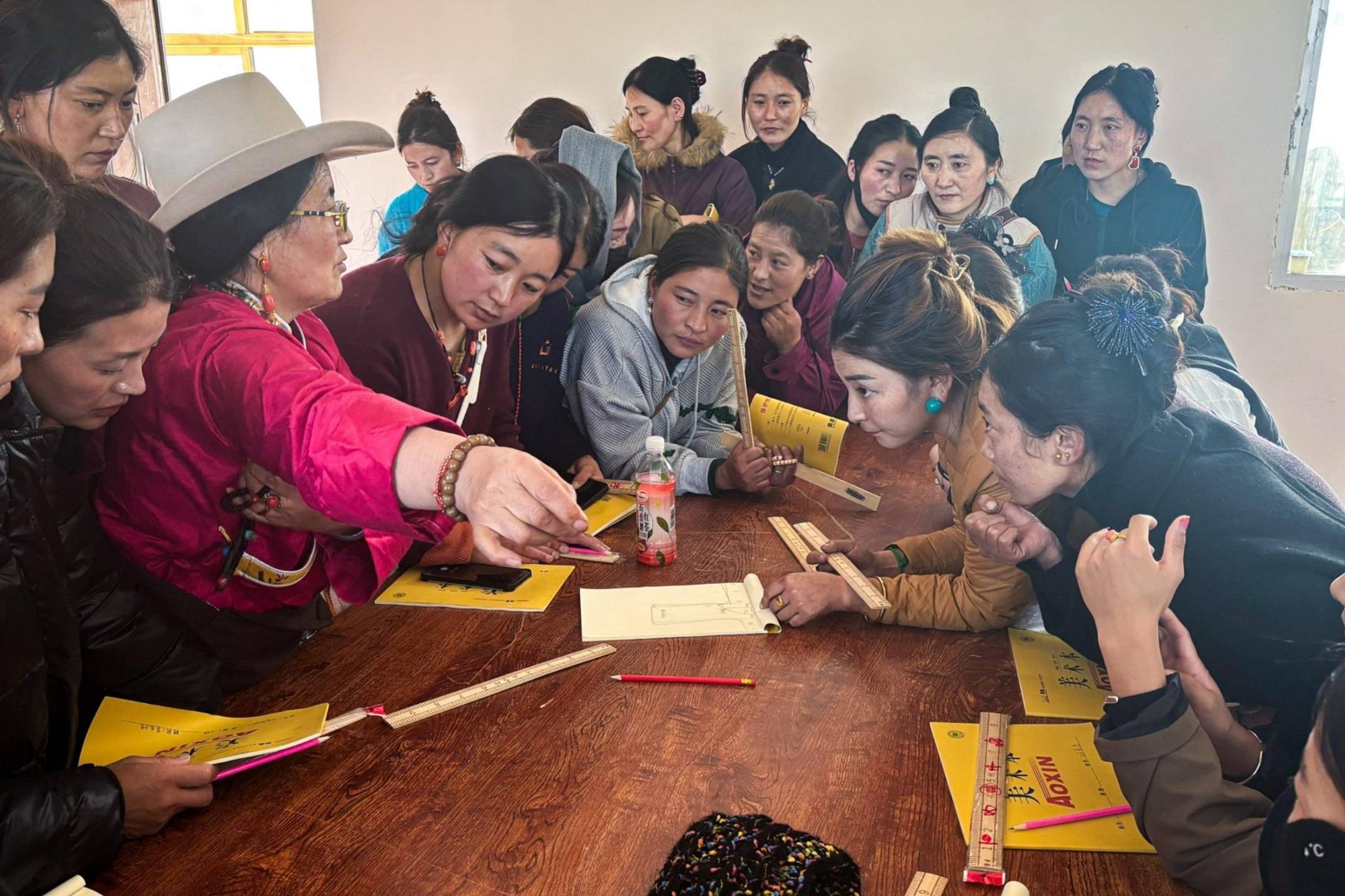 Women are seated around a table with papers, engaged in conversation and collaboration on a project or activity.