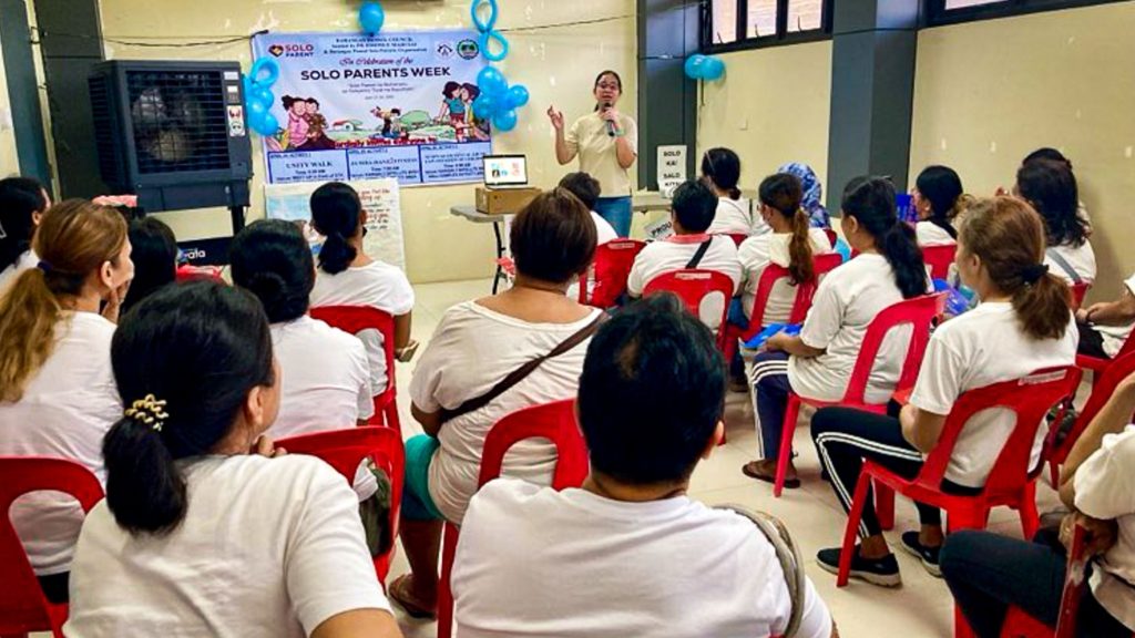 A group of people seated in chairs, attentively listening to the woman facilitating a seminar.