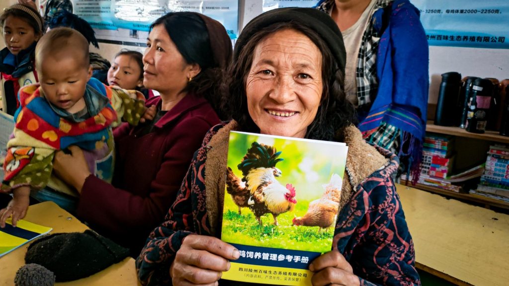 A woman holds a book featuring an illustration of a chicken on the cover, smiling as she engages with the content.