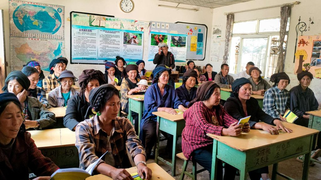A group of people seated in chairs attentively listening to a presentation in a classroom.
