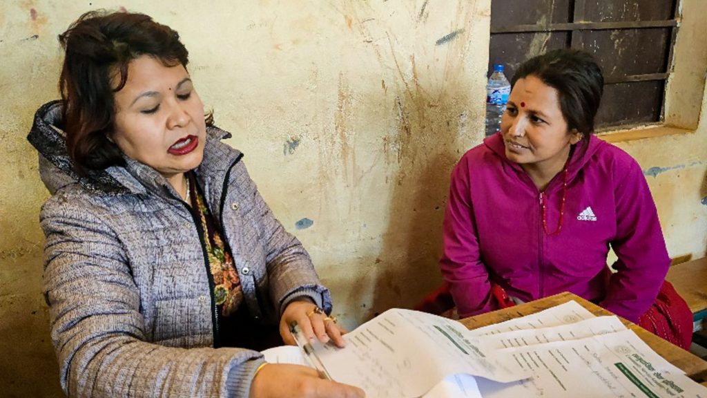 A doctor and patient sit at a table in a rural setting, engaged in a conversation during a medical consultation.