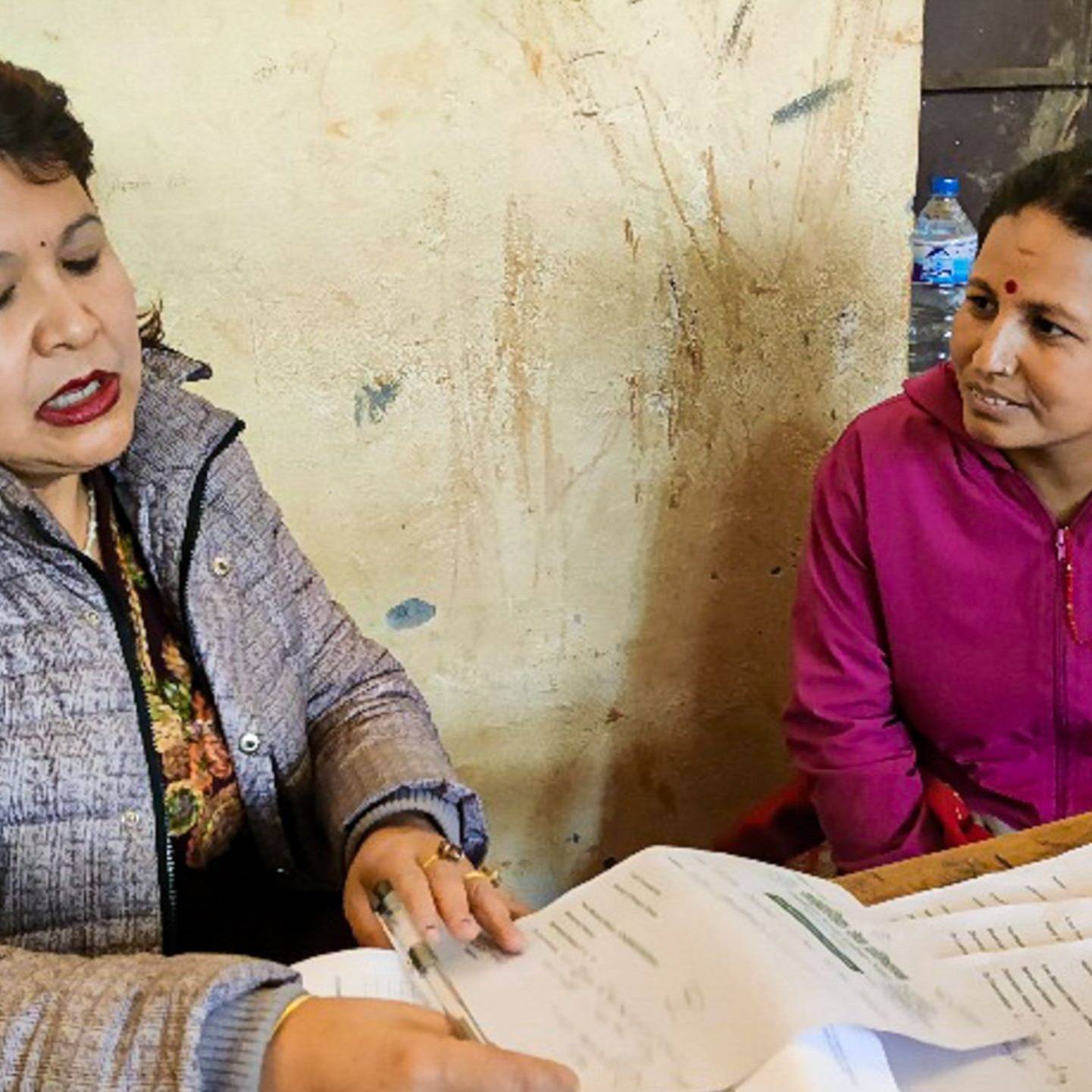 A doctor and patient sit at a table in a rural setting, engaged in a conversation during a medical consultation.