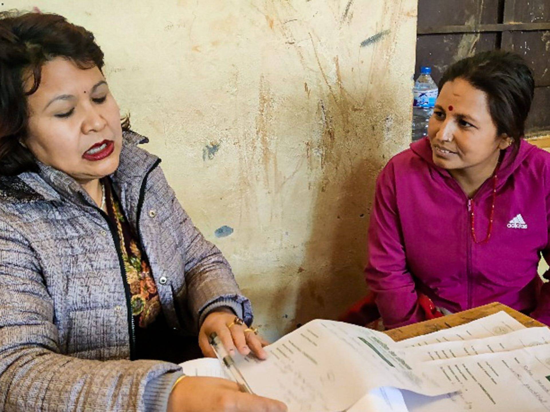 A doctor and patient sit at a table in a rural setting, engaged in a conversation during a medical consultation.