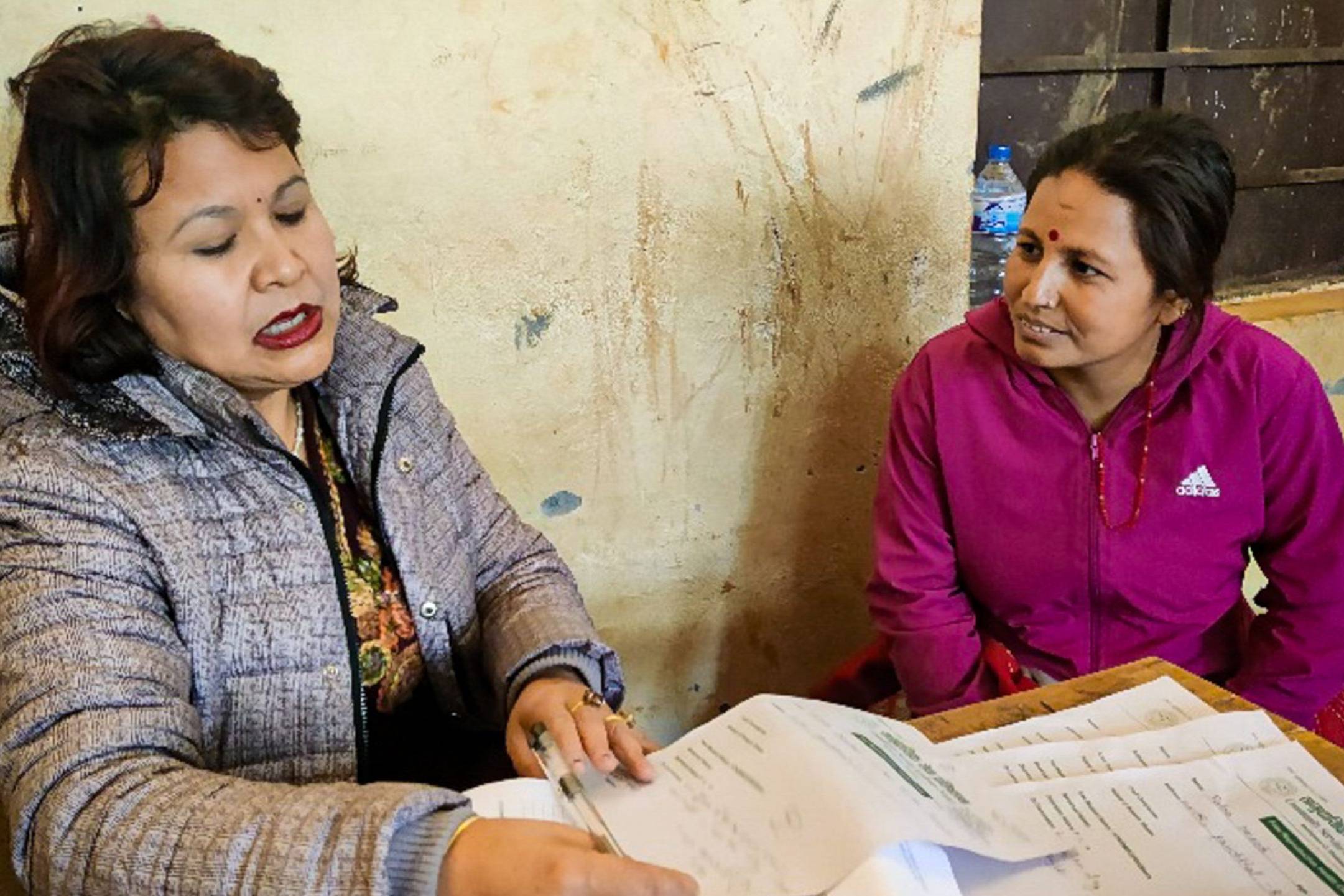 A doctor and patient sit at a table in a rural setting, engaged in a conversation during a medical consultation.