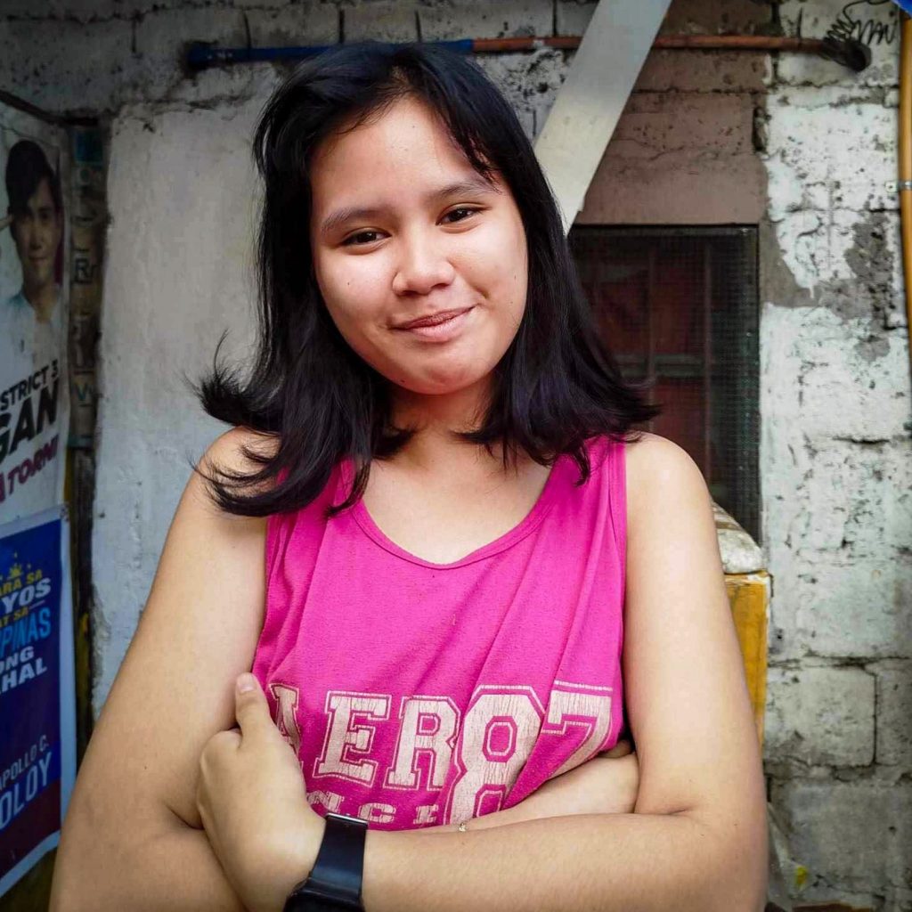 A woman in a pink tank top stands confidently.