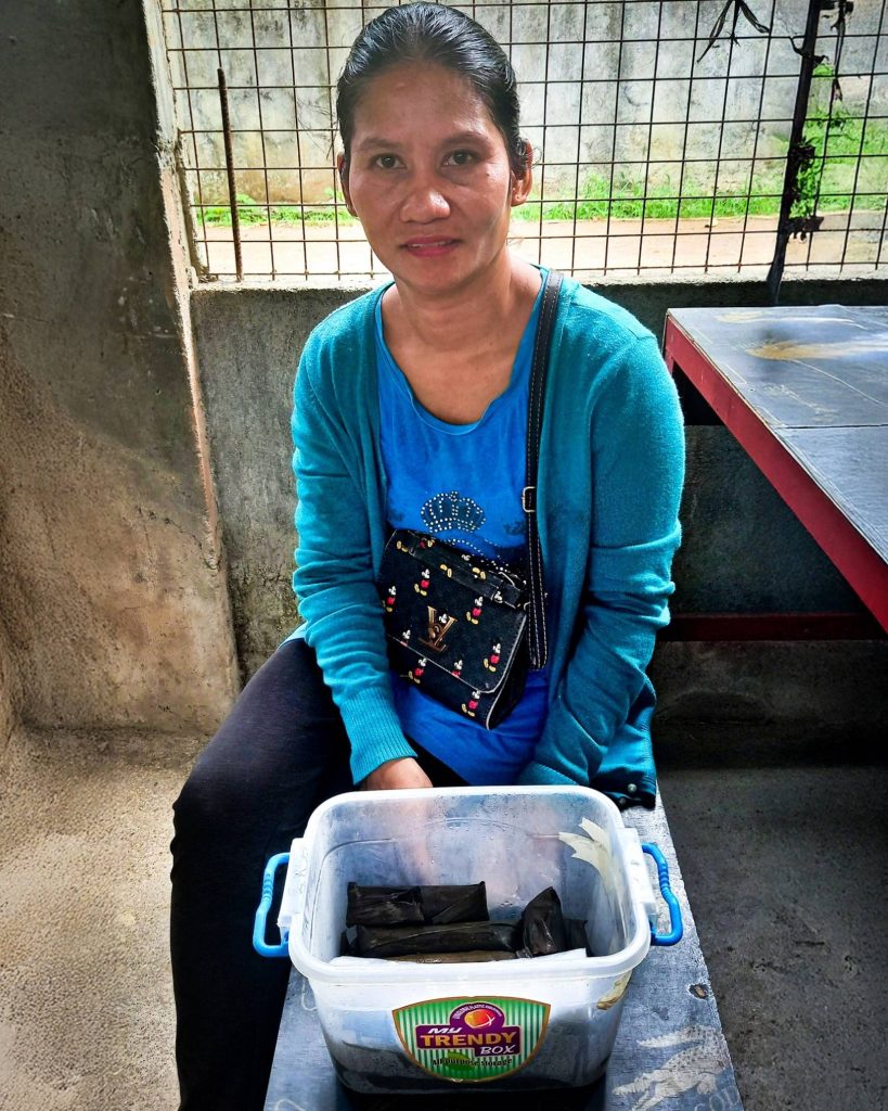 A woman sits on a bench, holding a bucket of food.